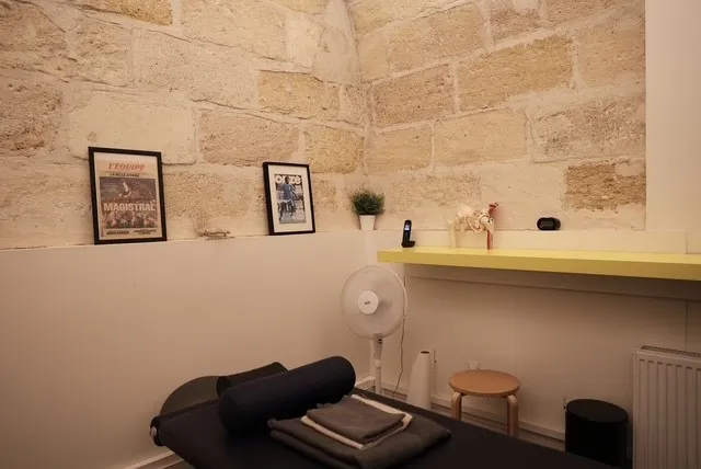 Un autre angle de la salle : le mur de pierre, un bureau et des unes sportives encadrées.